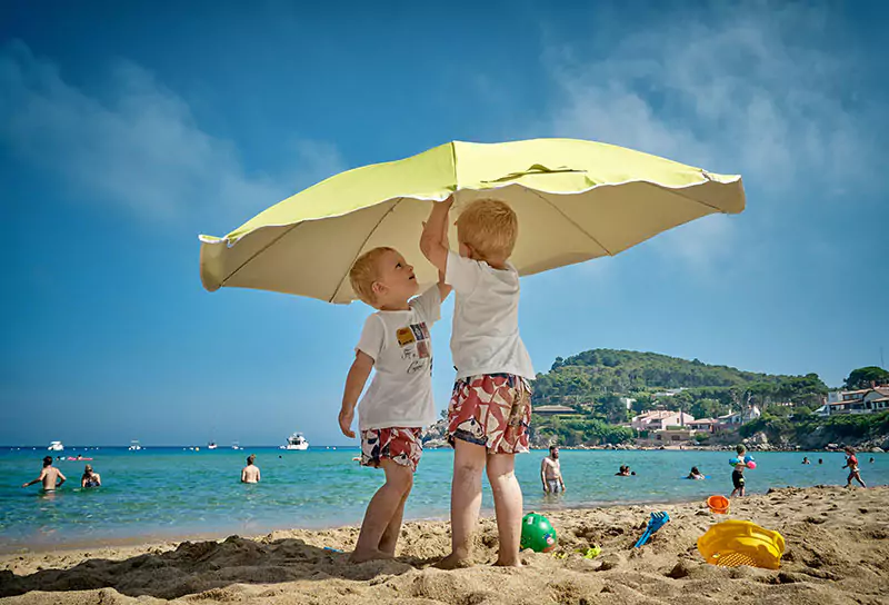 two child holding umbrella at the beach